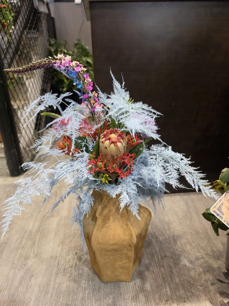 Composición exótica con protea, coral y foliaje azul en jarrón artesanal